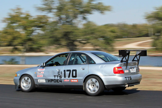 Image of the 9livesracing Audi S4 (b5) 1998-2001 big wang kit. The wing features a large white spoiler with black mounts for maximum downforce and low drag. The brown, partially-damaged rear portion of the car is shown. "Pre-order pricing" text is in the bottom left corner. Nine Lives Racing logo in the bottom right.
