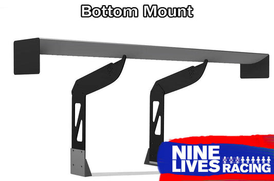 The 9livesracing Camaro Wang 2016+ 6th Gen Chassis Mount features two black, adjustable supports with a grey "Bottom Mount" wing. The Nine Lives Racing logo, displaying white text and a line of nine stick figures, is situated in the bottom right corner against a red and blue background. This design optimizes downforce for GT3 performance.