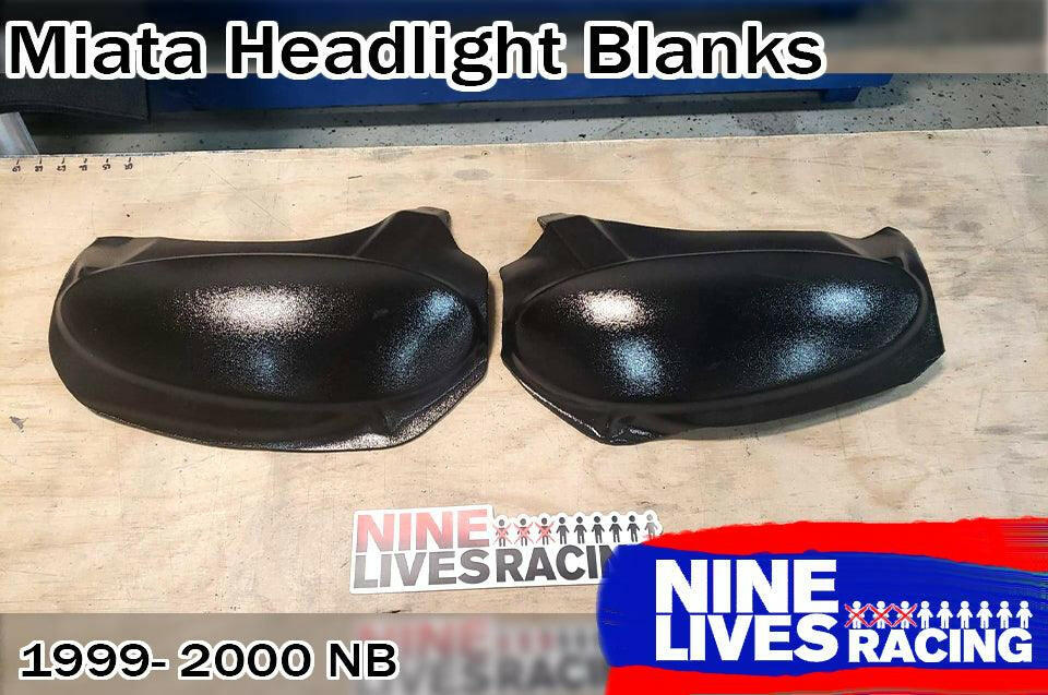 Two black Miata Headlight Blanks NB1-Only, crafted from robust ABS plastic for 1999-2000 NB models, are displayed on a wooden surface. The top text reads "Miata Headlight Blanks" and "1999-2000 NB." The logo of Nine Lives Racing is prominently featured in blue and red at the bottom right.