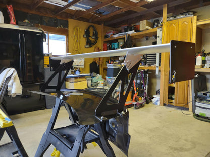 The Evolution 10 Big Wang kit, by 9livesracing, features a large aluminum wing that generates significant down-force and is mounted on a black trunk lid in a cluttered garage. Shelves and tools are visible in the background, along with a black refrigerator and wooden cabinets. The garage appears to be a workspace for car modifications.