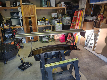 A cluttered garage with tools, shelves, and various items. In the center, a large black Evolution 10 Big Wang kit by 9livesracing is being worked on, placed on a sawhorse with a power drill nearby. A red ladder leans against the back wall, and various storage boxes are visible on the shelves.