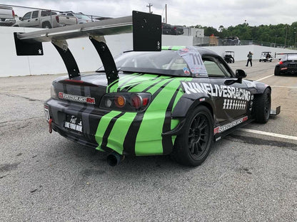 A race car with a prominent rear wing and a green-and-black striped design is parked in the pit area. The number "711" is displayed on the side window. The car features various decals, including "9livesracing" on the rear fender and "Speed Freaks USA" on the bumper, enhancing its downforce with sleek end plates from The Big Wáng!