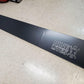 A long, black C10 1967-72 Truck spoiler Kit made from 6061 aluminum with a matte finish is positioned diagonally on a beige tiled floor. The spoiler, designed to enhance downforce, features the text "9livesracing" in white, accompanied by a silhouette of a person with outstretched arms.