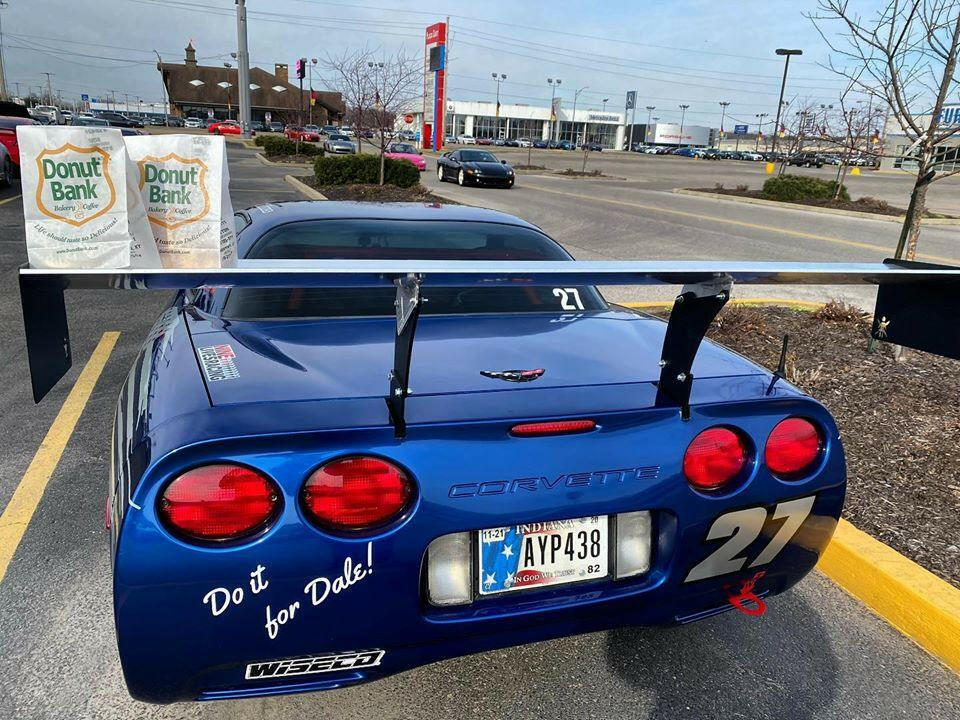 A blue Corvette Big Wang Chassis Mount ’97-13 C5/6 from 9livesracing is parked in a parking lot. The license plate reads "AYP438." The back of the car has decals with the number 27 and the text "Do it for Dale!" Sporting extruded aluminum wings, this Big Wang GT3 beast proudly bears two Donut Bank bags on its roof.