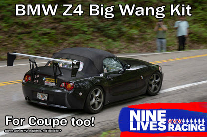 A black BMW Z4 equipped with a Big Wang Kit is navigating a winding road. The text on the image reads, "BMW z4 Big Wang Kit. 2003-08 (E85)," "For Coupe too!" and "9livesracing." There is a blurred figure in the background, and trees line the road.
