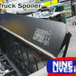 Image of a 60-inch wide C10 1967-72 truck spoiler kit made from sturdy 6061 aluminum installed on a vehicle. The spoiler features "9livesracing" and a logo on it. The text "C10 Truck Spoiler Kit" is at the top left, and "60'' wide" is at the bottom left. The workshop setting has various tools and equipment in the background.