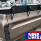 Image of a Chevrolet truck's rear view featuring a black spoiler attached to the tailgate. Text on image: "C10 1967-72 Truck Spoiler Kit", "9livesracing", and "60” wide". The 6061 aluminum spoiler is designed to boost downforce. The truck is parked in a workshop with various tools and equipment visible.