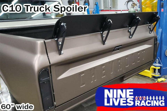 Image of a Chevrolet truck's rear view featuring a black spoiler attached to the tailgate. Text on image: "C10 1967-72 Truck Spoiler Kit", "9livesracing", and "60” wide". The 6061 aluminum spoiler is designed to boost downforce. The truck is parked in a workshop with various tools and equipment visible.