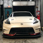 A white sports car, probably a Nissan 370Z, is parked inside a garage with its front facing the camera. The car showcases sleek headlights, a prominent front grille, and red accents on the lower bumper. A 9livesracing 370z Rocket Nose v2 Splitter ’08-20 Z34 enhances its aerodynamic downforce while various tools and equipment are visible in the background.