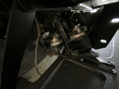 Close-up of the Corvette Splitter - C6 & C5 ‘05-13 by 9livesracing, showcasing metal brackets, bolts, and intertwined wires. The components feature precision CNC cut pockets and low friction polymer surfaces, all meticulously connected and arranged within a dark, confined space, likely integral to a larger machine or vehicle. Dim lighting accentuates the metallic surfaces of these high-quality parts.