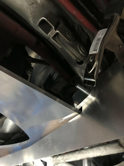 A close-up view shows a Miata Diffuser '90-05 NA/NB by 9livesracing being clamped in place with a tool. The diffuser is part of an assembly or structure, with a screw and some mechanical components visible in the background. There is a barcode sticker on the clamp.