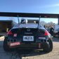 A black sports car with a massive 9livesracing pre-preg carbon wing and various decals, including Motul and StopTech, is parked on a paved area. The license plate reads "RNL7135" from Georgia. A helmet is resting on the rear of the car, and a secondary car is visible nearby.