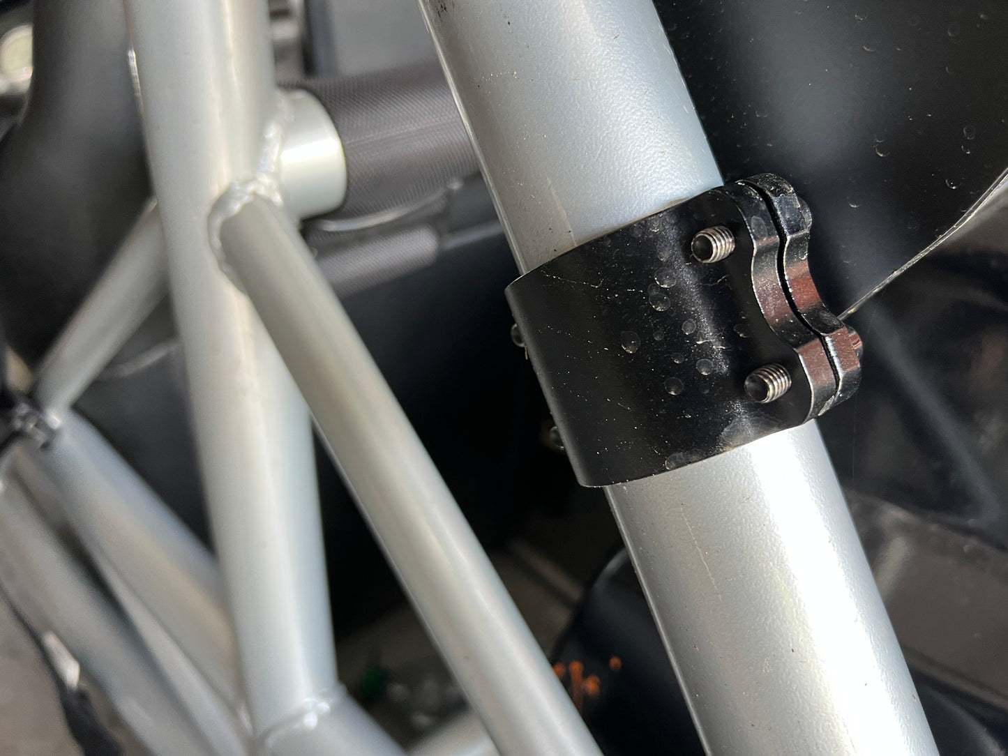 A close-up view of the Exocet v2 Big Wang Kit by 9livesracing showcases light gray cylindrical bars connected by a black clamp with bolts. The industrial setting emphasizes the robust, utilitarian construction that mirrors the down-force principles seen in GT3 performance engineering.