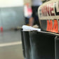 Close-up of the rear section of a vehicle, probably a car, highlighting the Miata Diffuser '90-05 NA/NB by 9livesracing with a small piece of crumpled white paper lodged in it. The background is out-of-focus, featuring people and some equipment.