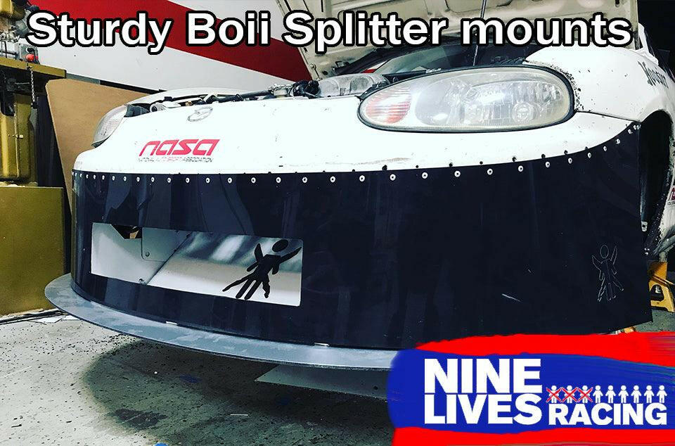 A close-up of a car's front bumper with a Miata Sturdy Boii Splitter Mounts '90-05 NA/NB attached. The splitter is secured with multiple screw mounts for enhanced downforce. The bumper features a NASA logo and cartoon characters. The image is branded with the "9livesracing" logo in the bottom right corner. Text at the top reads "Sturdy Boii Splitter mounts.