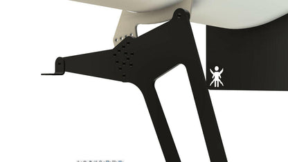 Close-up of a black, angular metal bracket attached to a structure, optimized for the Civic Hatch EF Wang kit 88-91 by 9livesracing to enhance down-force. The bracket features multiple small circular holes and has a protruding part at the end. In the background, a white and black area with a small white pictogram resembling a person can be seen.