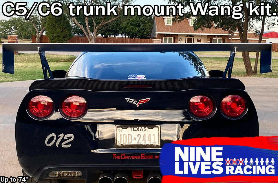 Photograph of a black Chevrolet Corvette featuring a Texas license plate JDD-2441 and adorned with a substantial Nine Lives Racing aluminum wing mounted on the trunk. The vehicle displays the number "012" on its bumper. The top of the image showcases "Corvette Big Wang Trunk Mount Kit '97-13 C5/6," while the bottom right corner bears the 9livesracing logo.