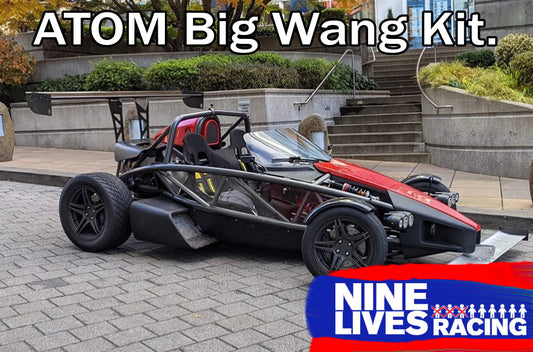 A sleek black and red Ariel Atom sports car is parked outdoors near concrete stairs and modern buildings. The text "Ariel Atom Big Wang" appears at the top, highlighting its enhanced airfoils for an optimized lift-to-drag ratio. "9livesracing" is displayed at the bottom right with a logo featuring nine tiny car icons.