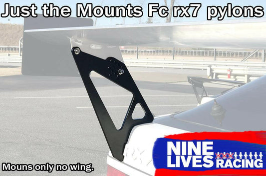 A car is equipped with an aftermarket aluminum Fc Rx7 Wing Mounts - Pylons Only kit by 9livesracing. These mounts are designed to support a spoiler, but the spoiler is not present. The background shows an empty road and a safety barrier. The text reads, "Just the Mounts FC Rx7 pylons" and "9livesracing".