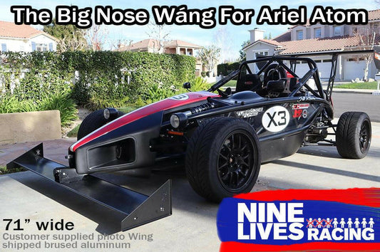 A black Ariel Atom race car with red and white accents sits in a driveway. It boasts a large extruded aluminum front wing, the Ariel Atom Big Nose Wang '00+, measuring 71 inches wide, enhancing its lift-to-drag ratio. Text at the top reads "The Big Nose Wang For Ariel Atom," and the bottom right corner displays the "9livesracing" logo.