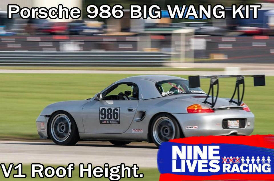 A silver Porsche Boxster 986 with a large rear spoiler races on a track, showcasing its impressive down-force. The car sports the number 986 on its side. The text overlay reads, "Porsche Boxster Big Wang Kit '96-04" and "V1 Roof Height." A "9livesracing" logo graces the bottom right corner.