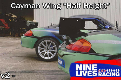 Two green sports cars with open rear wings are parked side by side outside a garage. The text at the top reads "Cayman Wing 'Half Height'" and a "9livesracing" logo is at the bottom right corner. Featuring extruded aluminum wings for enhanced down-force, "v2" is noted in the bottom left corner.