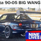 A blue Mazda Miata with a large rear wing is shown parked on a road. The car, enhanced with the Miata Big Wang Kit '90-05 NA/NB for optimal down-force, sports racing decals and a license plate reading "590-95." Text at the top reads "Miata Big Wang Kit '90-05 NA/NB," with a 9livesracing logo at the bottom right corner.
