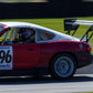 A Miata Diffuser '90-05 NA/NB from 9livesracing, installed on a red and white race car with the number 96 on the door and an aluminum rear wing, is speeding on a track. The V8 Miata displays visible sponsor decals. The driver, partially visible through the window and wearing a helmet, adds to the dynamic scene as the blurred background emphasizes their motion.