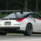 The 350z Big Wang Kit '02-08 Z33, by 9livesracing, transformed a modified sports car bearing the number 50 on its door and equipped with a substantial rear wing crafted from extruded aluminum wings, decals, and a wide body kit. The sleek white car is accented in red and black as it charges around the racetrack. Blurred greenery in the background signals high speed, highlighting its impressive Big Wang GT3 performance.