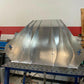 A partially constructed aluminum ventilation unit with several connected panels rests on a perforated workbench. The background shows a red and white wall with various tools and equipment scattered. Electrical cords and other workshop items, including bits from a 9livesracing Miata Diffuser '90-05 NA/NB project, are visible on the floor.