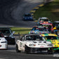 Several race cars rounding a corner on a racetrack, featuring an NB Miata fitted with the 9livesracing Miata Medium Downforce Kit '90-05 NA/NB in the forefront, closely followed by other brightly colored cars. Trees and a curving track are visible in the background. The image has the hashtag #GRIDLIFE and includes the photographer's name.