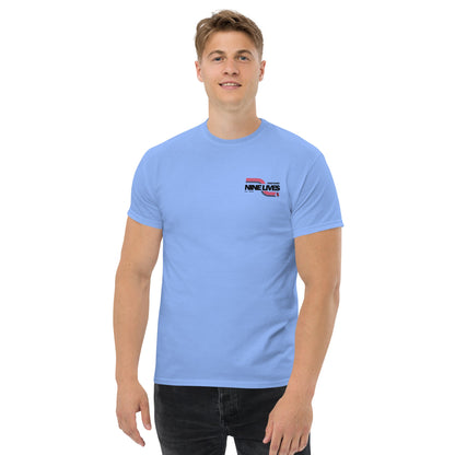 A young man with light brown hair stands against a plain white background, wearing a light blue Men's Soda Can Wang t-shirt from Nine Lives Racing. The 100% cotton shirt pairs perfectly with his dark jeans, making it ideal for layered streetwear outfits. He smiles with his arms relaxed by his sides.