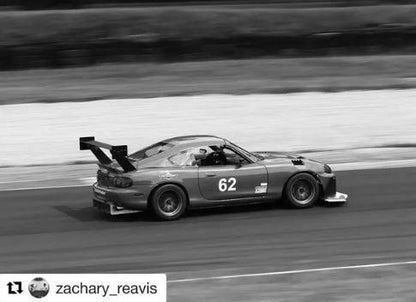 Black and white image of a race car with the number 62, driving on a race track. The 9livesracing Miata Big Wang Kit '90-05 NA/NB enhances its prominent rear wing, optimizing down-force as it appears to be in motion. The Instagram username "zachary_reavis" is visible in the bottom left corner.
