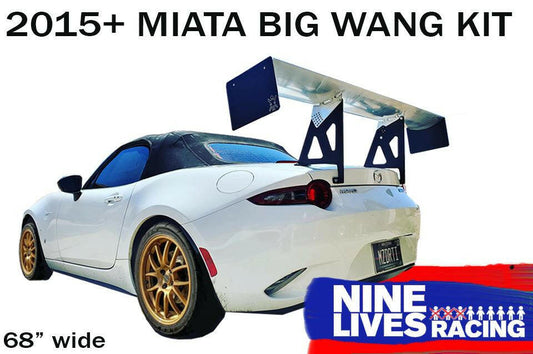 A white convertible car with a black soft top is fitted with an aftermarket high down-force wing on the rear. The text reads "Miata Big Wang Kit 2016+ ND" and "9livesracing." The car, featuring gold-colored wheels and a brand logo in the bottom right corner, boasts an aluminum airfoil for enhanced performance.