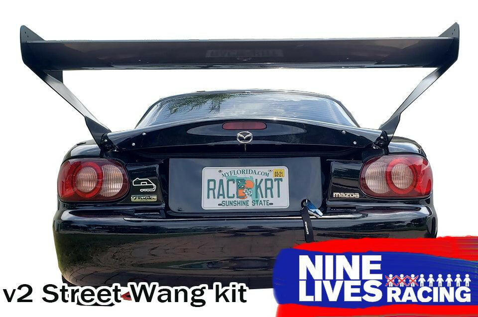 A rear view of a black Mazda features a prominently attached Miata V2 Street Wang '90-05 NA/NB measuring 48 inches. The Florida license plate reads "RAC3KRT," with visible stickers and a rear tow hook. The text at the bottom reads "v2 Street Wang kit" alongside the logo for 9livesracing, emphasizing its performance edge.
