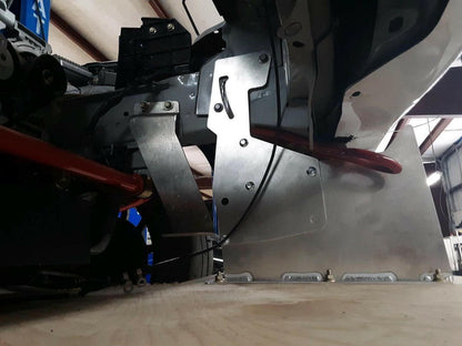 Low angle view of the interior mechanics of a vehicle, revealing various metallic components, cables, and part of the chassis. The image emphasizes 9livesracing's Miata Sturdy Boii Splitter Mounts '90-05 NA/NB amidst the intricate assembly and connections within the vehicle.