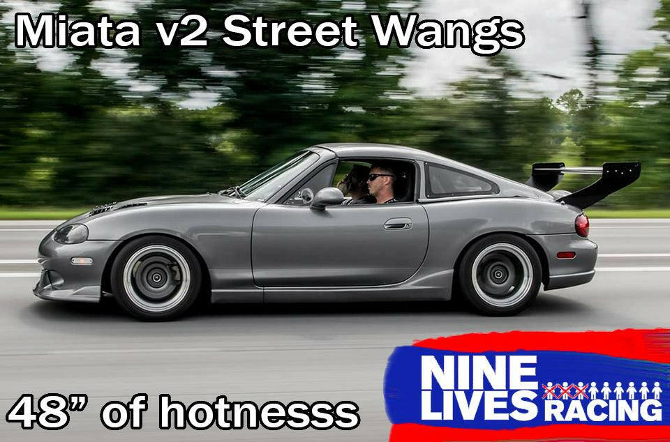 Side view of a gray sports car with a large rear wing, driving on a road with a blurred green background. Text reads "Miata V2 Street Wang '90-05 NA/NB" at the top, "48" of performance" at the bottom, and a "9livesracing" logo with red, white, and blue colors in the bottom right corner.