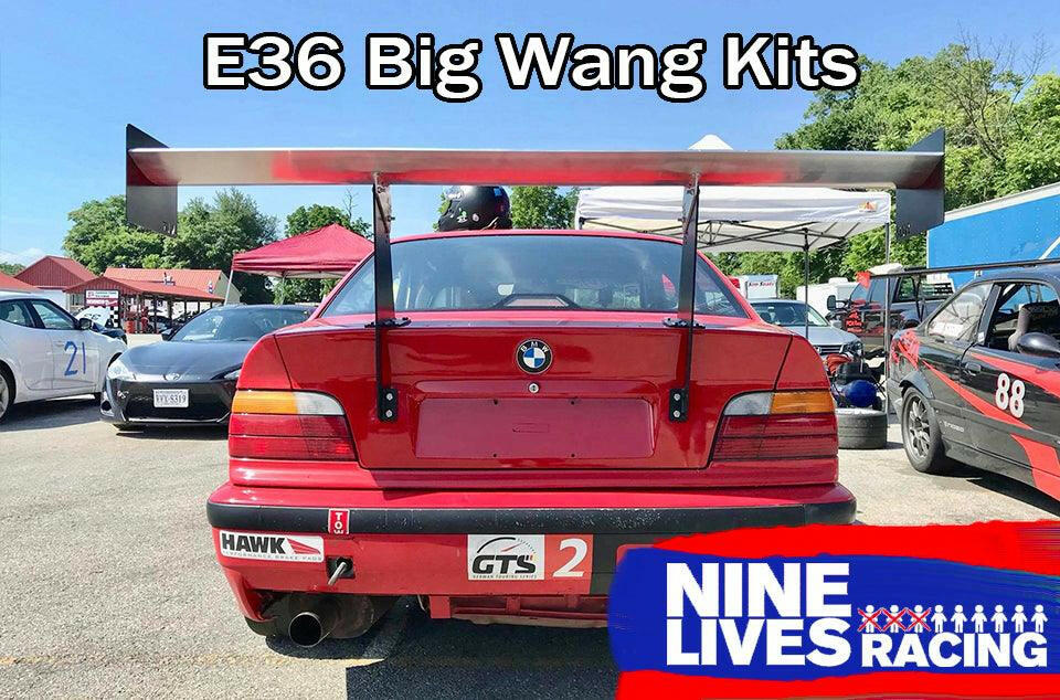 A red BMW E36 race car, equipped with a 3-Series Big Wang Kit '90-00 E36, parked in a paddock area during a motorsport event. There are other cars and tents in the background. Text at the top reads "E36 Big Wang GT3 Kits" and a logo in the bottom right corner says "9livesracing".