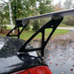 A close-up of a large rear spoiler mounted on the trunk of a black car. The 350z Big Wang Kit '02-08 Z33 by 9livesracing, crafted with extruded aluminum wings and black brackets, is set against a background of a wet driveway, fallen autumn leaves, and trees.