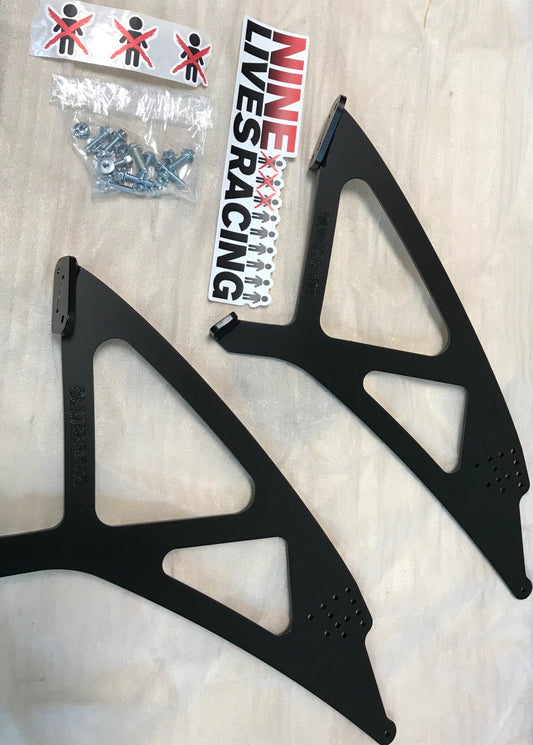 Two black metal brackets, a pack of screws, and a "9livesracing" sticker are laid out on a white surface. The 350z Big Wang Kit '02-08 Z33 Mounts/Pylons Only offers easy installation with options for powder coat upgrades.